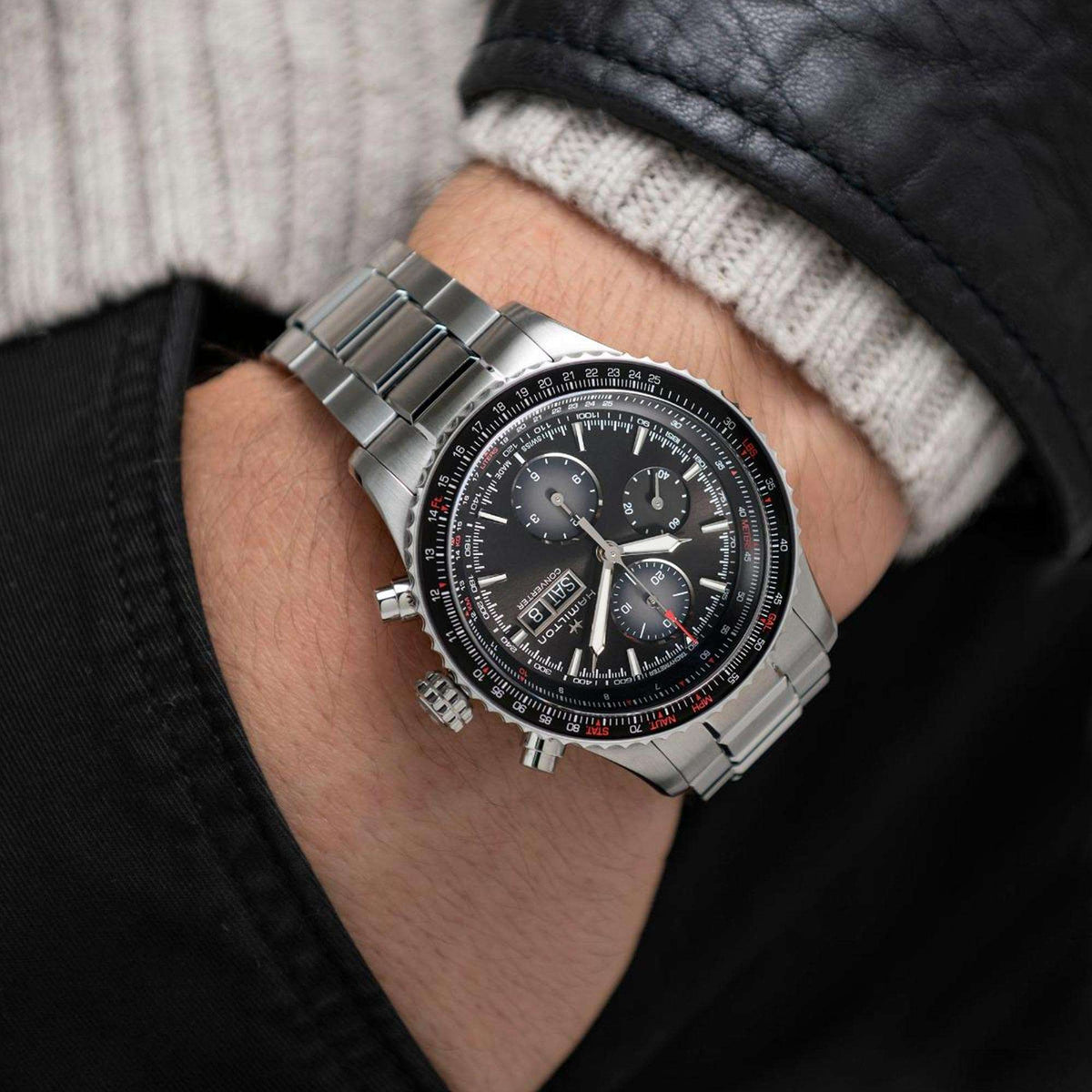 Men's stainless steel chronograph watch on wrist with black dial and red bezel markings.