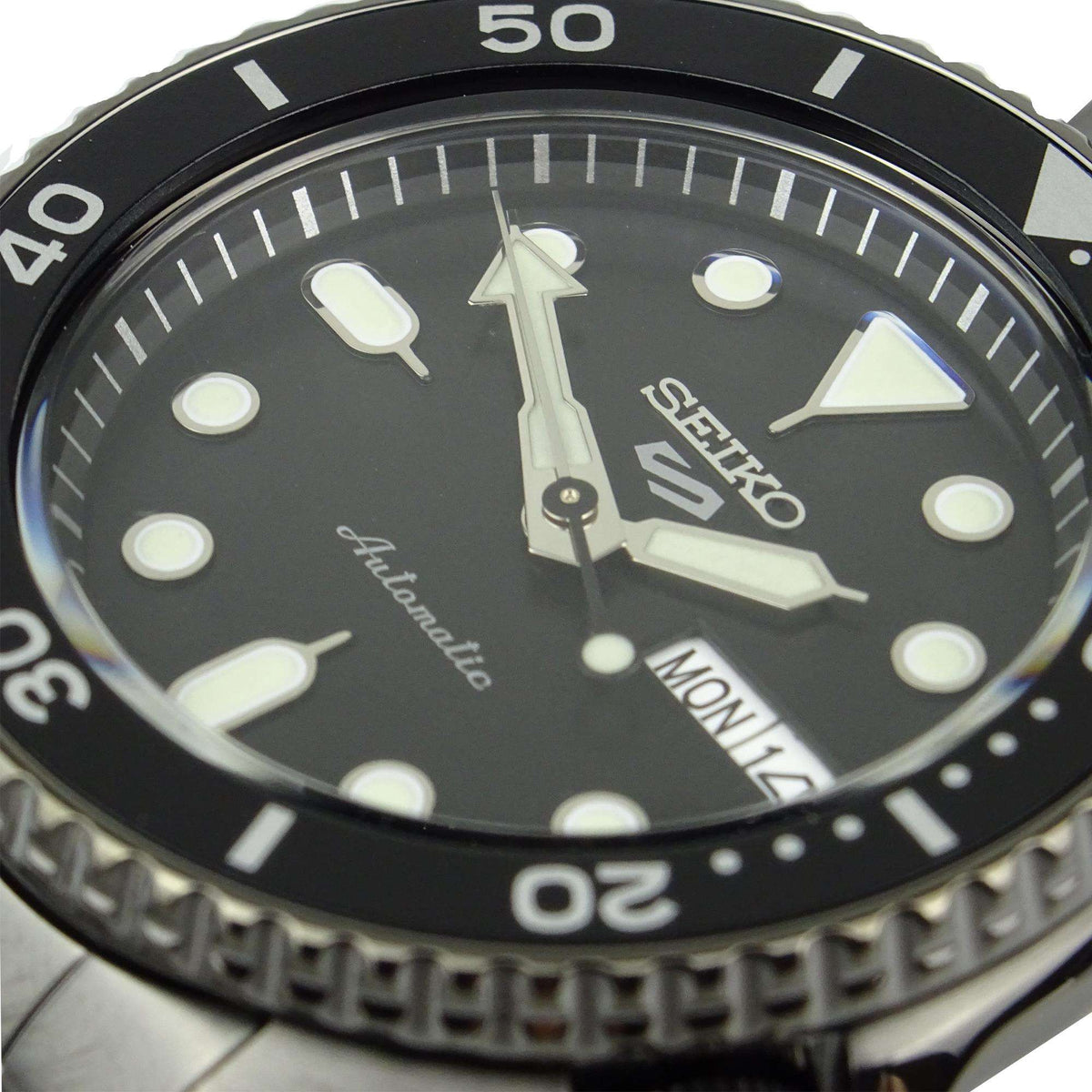 Close-up of men's black dial automatic watch with luminous markers and bezel numerals