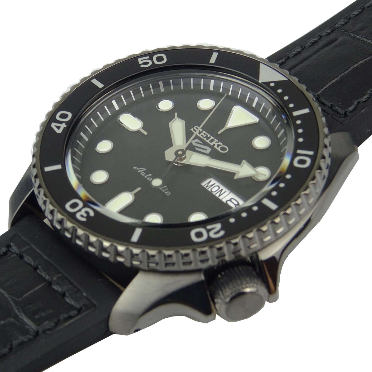 Men's automatic watch close-up on black dial with date window (MON 8) and leather strap.