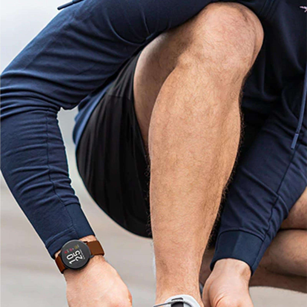 Smartwatch on wrist with black face and tan leather strap, showing time and icons