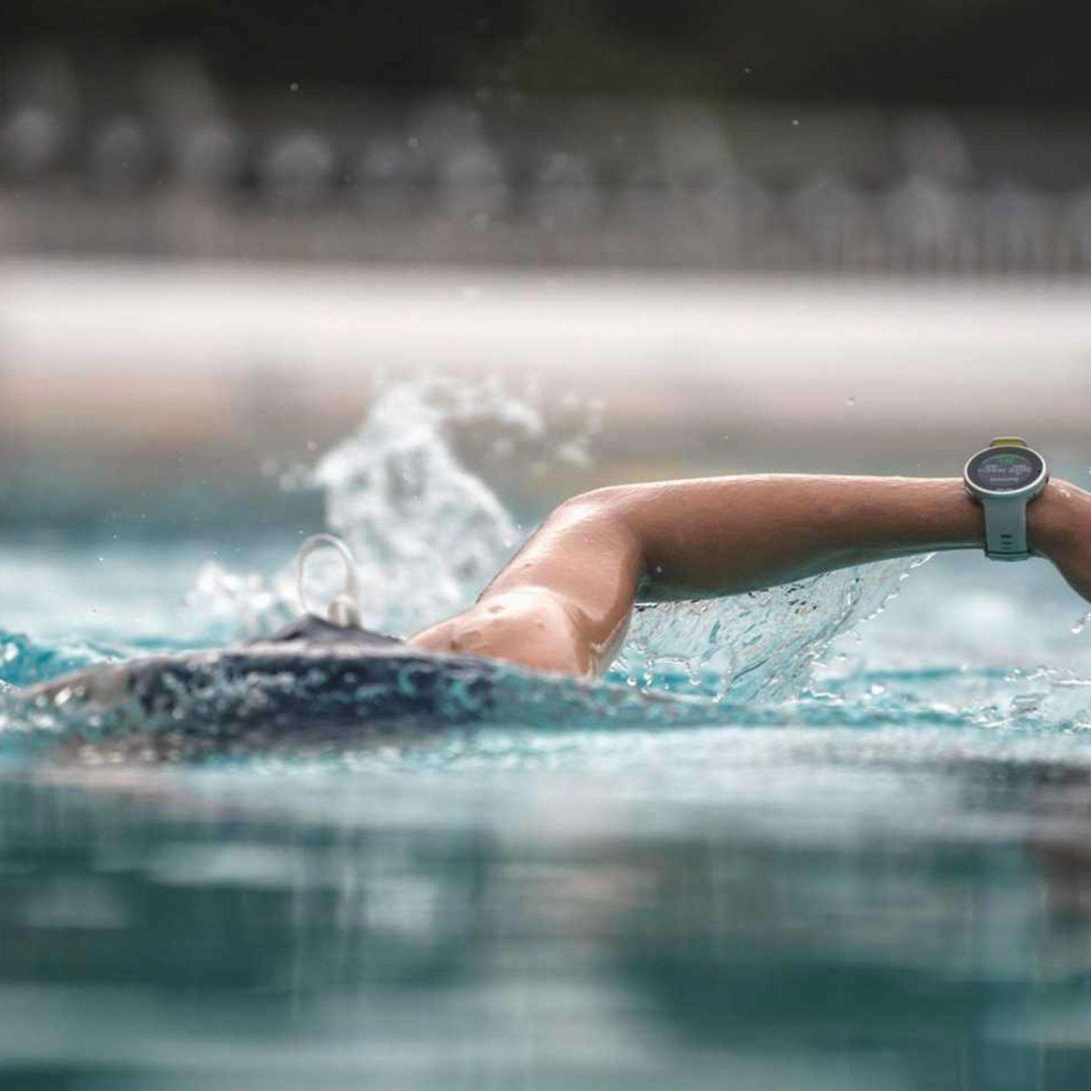 Smartwatch on wrist while swimming, showing dark display and grey rubber strap.