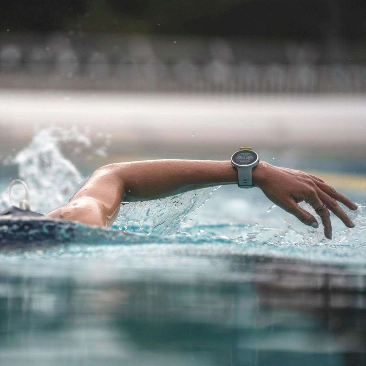 Grey rubber-strap smartwatch on swimmer's wrist above the water with screen visible