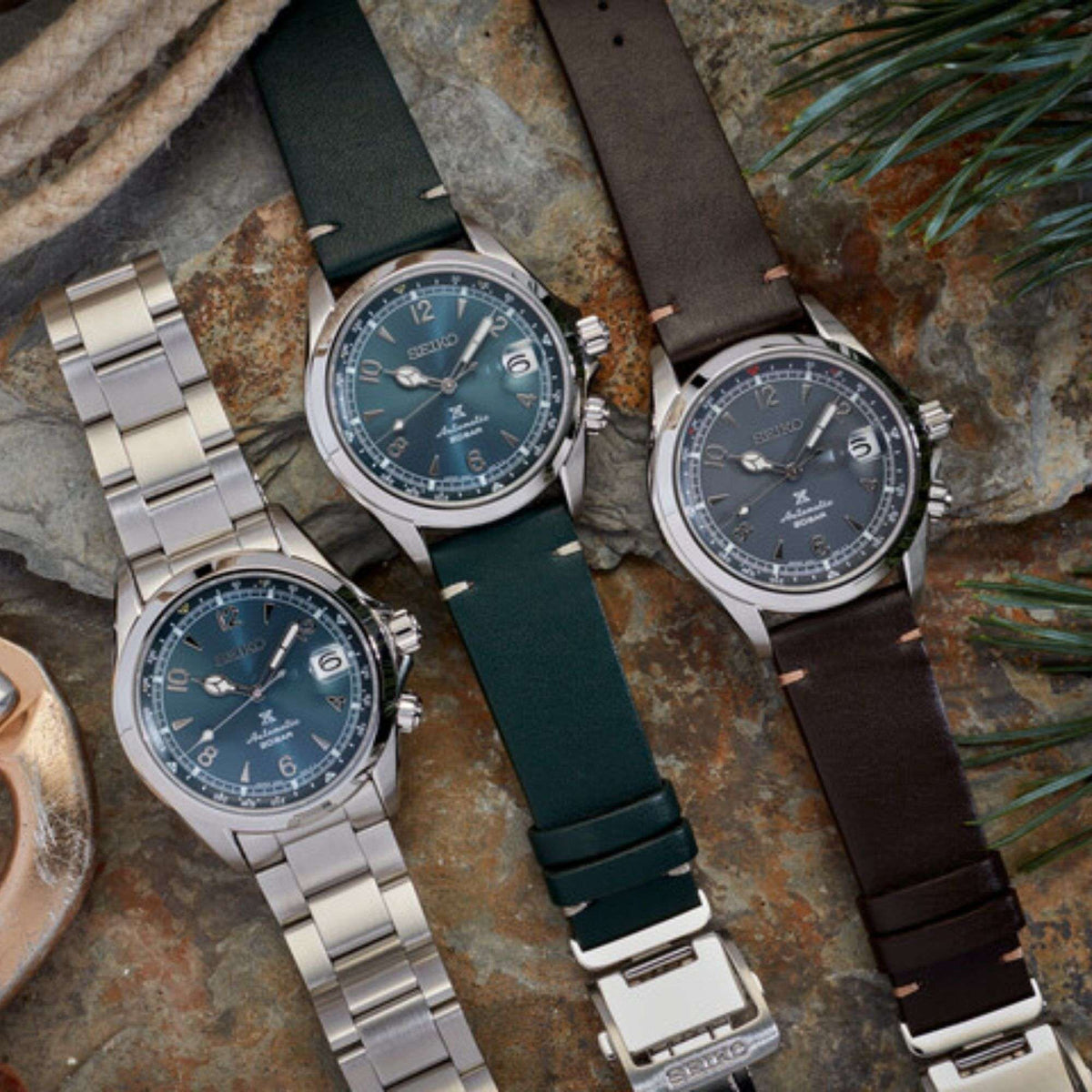 Three men’s automatic wristwatches with blue dials on metal, green and brown straps