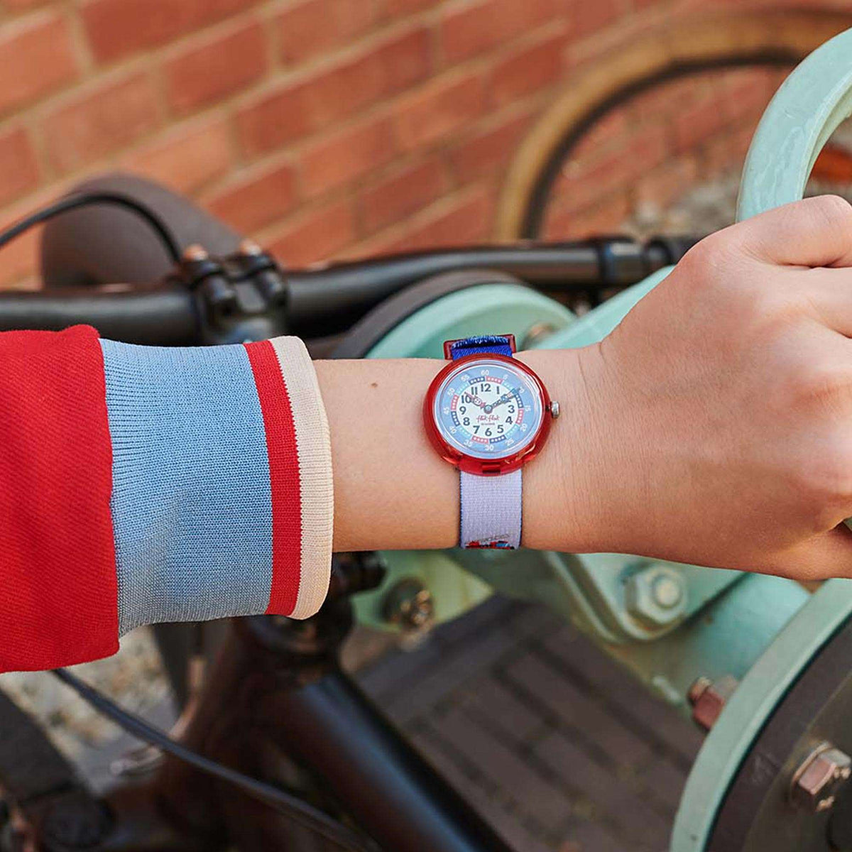 Kids watch on wrist with red case, blue dial, and light-blue textile strap