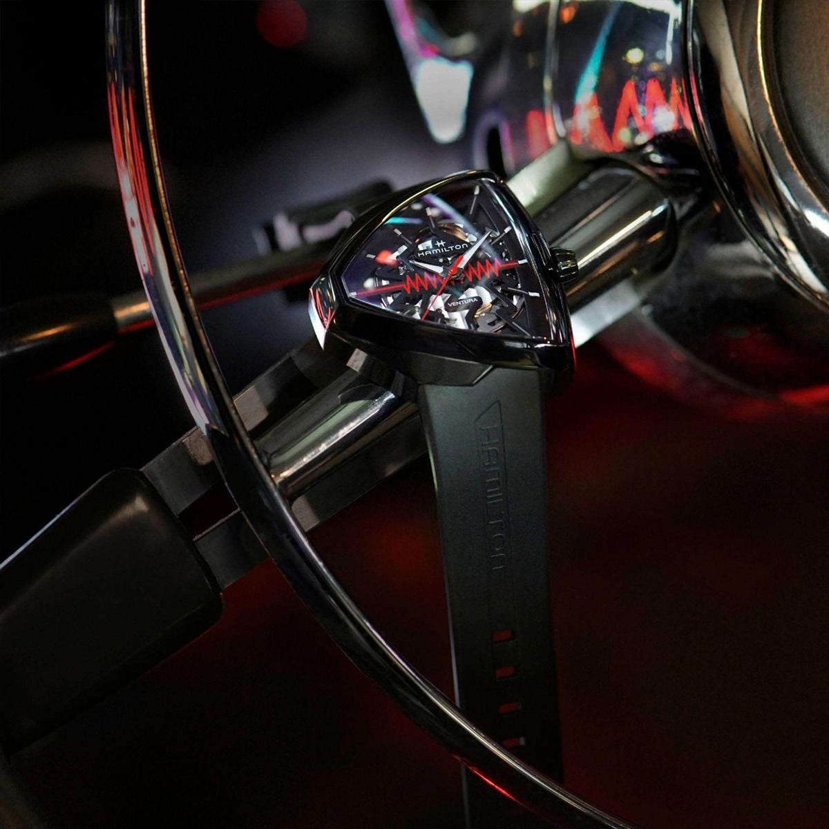 Black skeleton watch on black rubber strap, angled view with red zigzag seconds hand