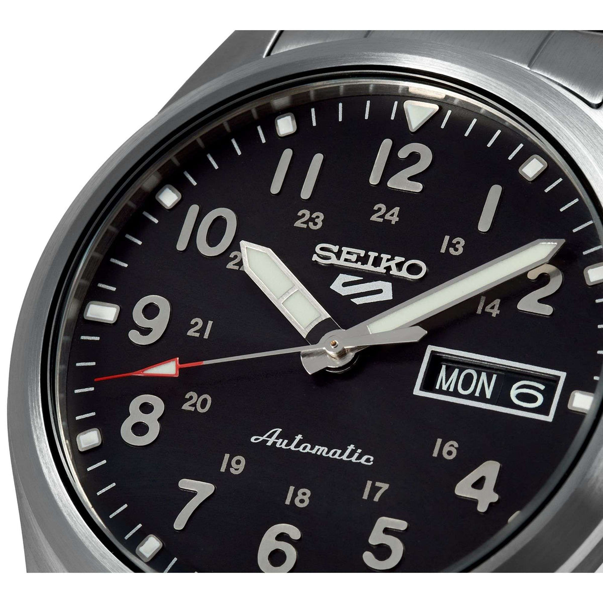 Close-up of Seiko 5 Sports watch face with black dial, luminous markers, and MON day window