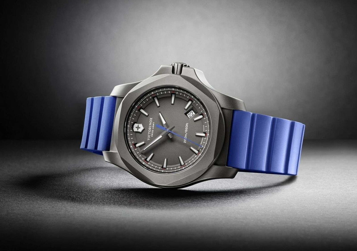 Men's wristwatch side view: blue rubber strap, grey titanium case, dark analog dial.