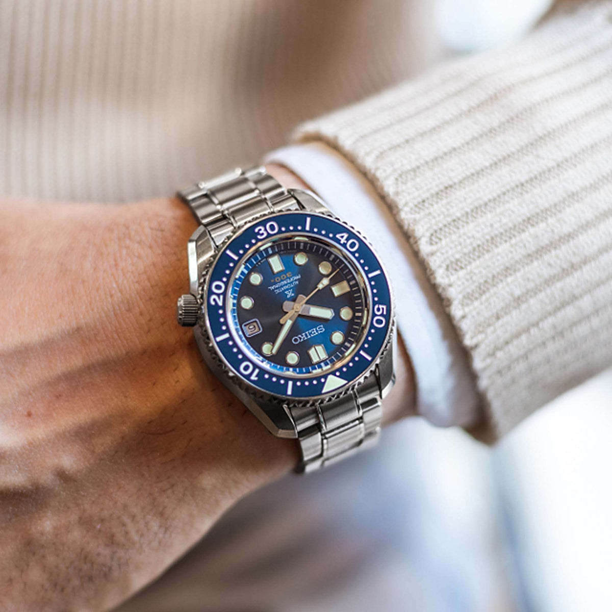 Blue-dial stainless steel diver watch on wrist with metal bracelet and round bezel