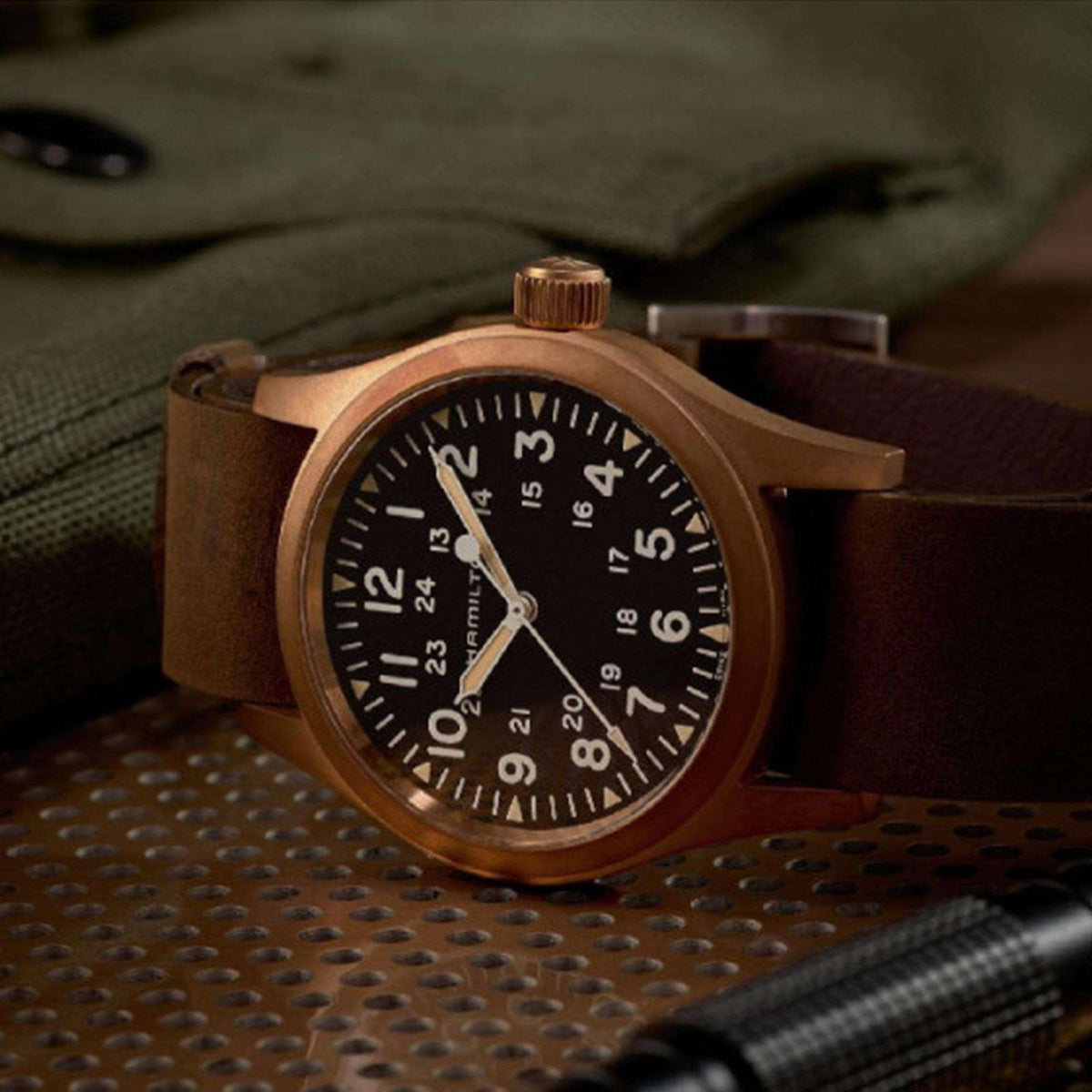Hamilton Khaki Field H69459530 mechanical military style watch angled perspective resting on textured surface with bronze case and black dial