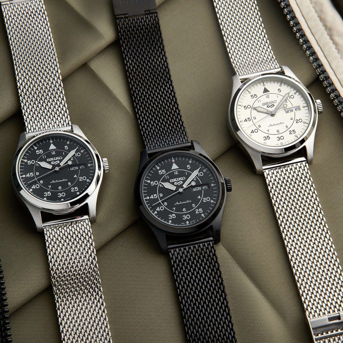 Three Seiko watches with different mesh straps on a textured surface