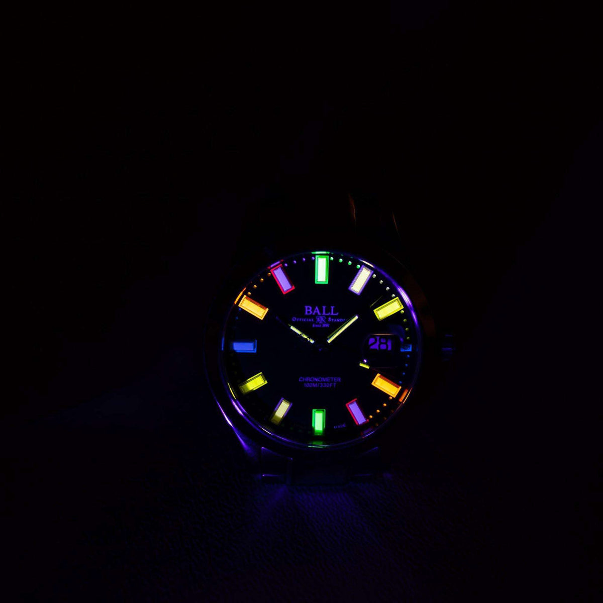 Men's watch dial close-up with glowing multicolor markers and date display on black face