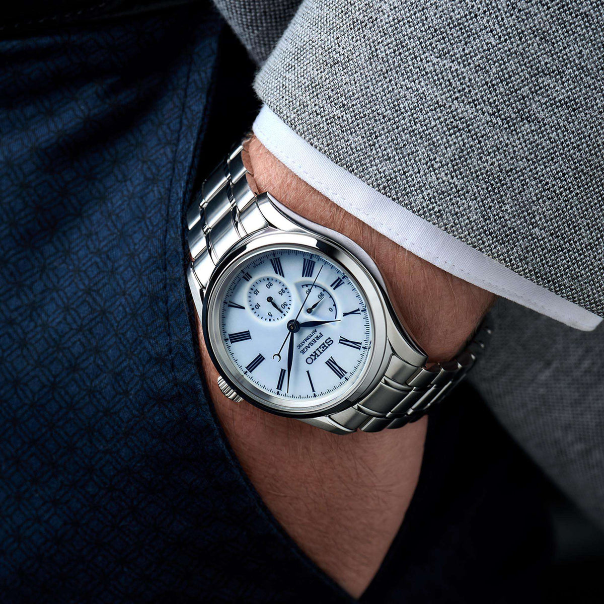 Men's automatic steel watch with blue dial and Roman numerals worn on wrist