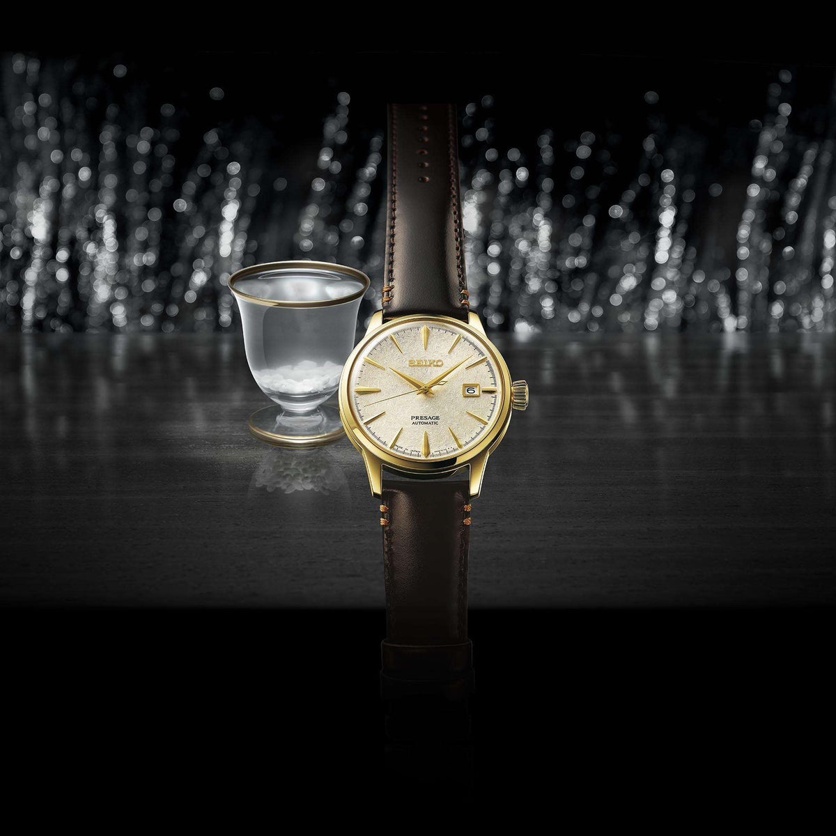 Seiko Presage Cocktail Time SRPH78J1 wristwatch with brown leather strap next to a glass on a dark background