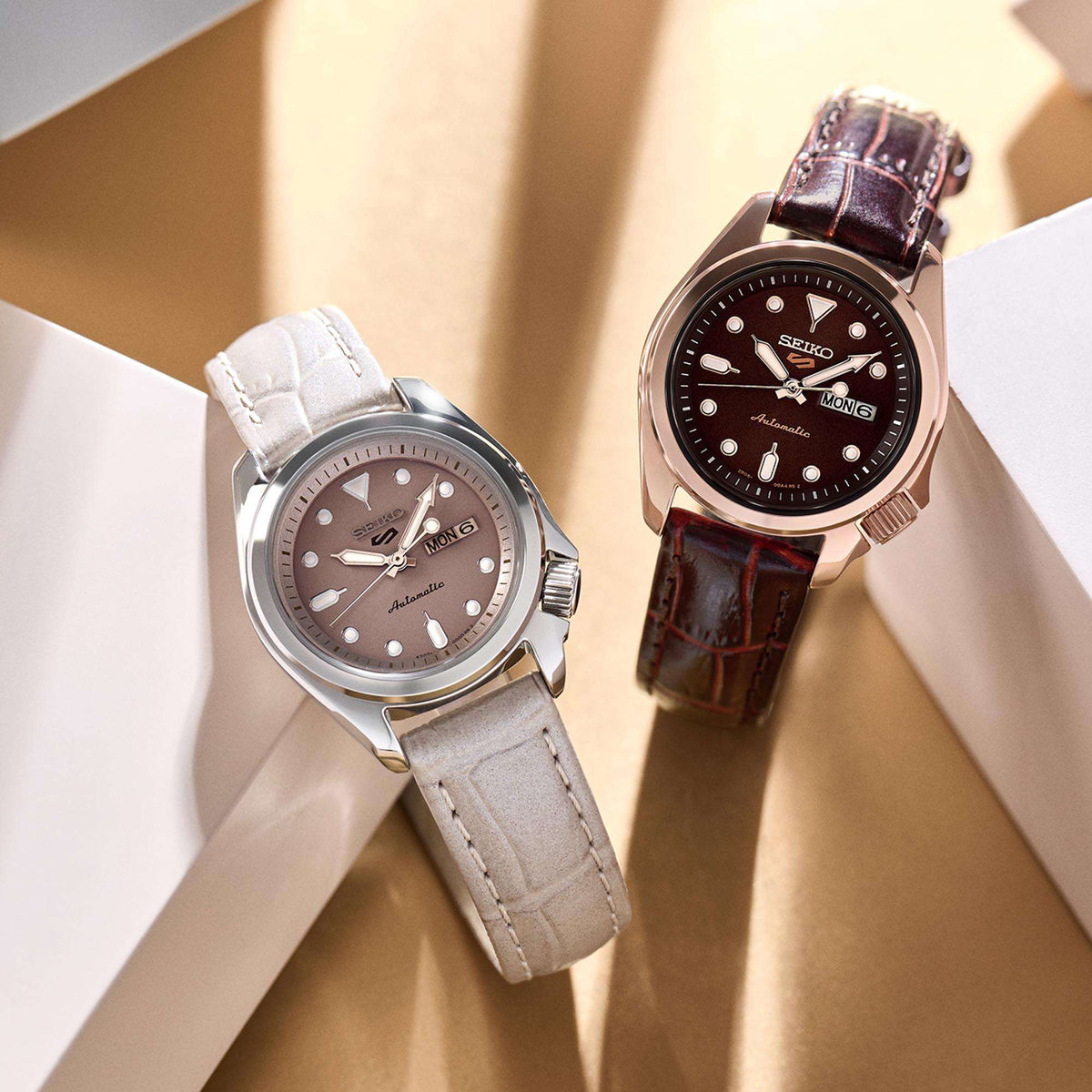 Two Seiko 5 ladies automatic watches: one dark dial with brown leather strap, one light dial