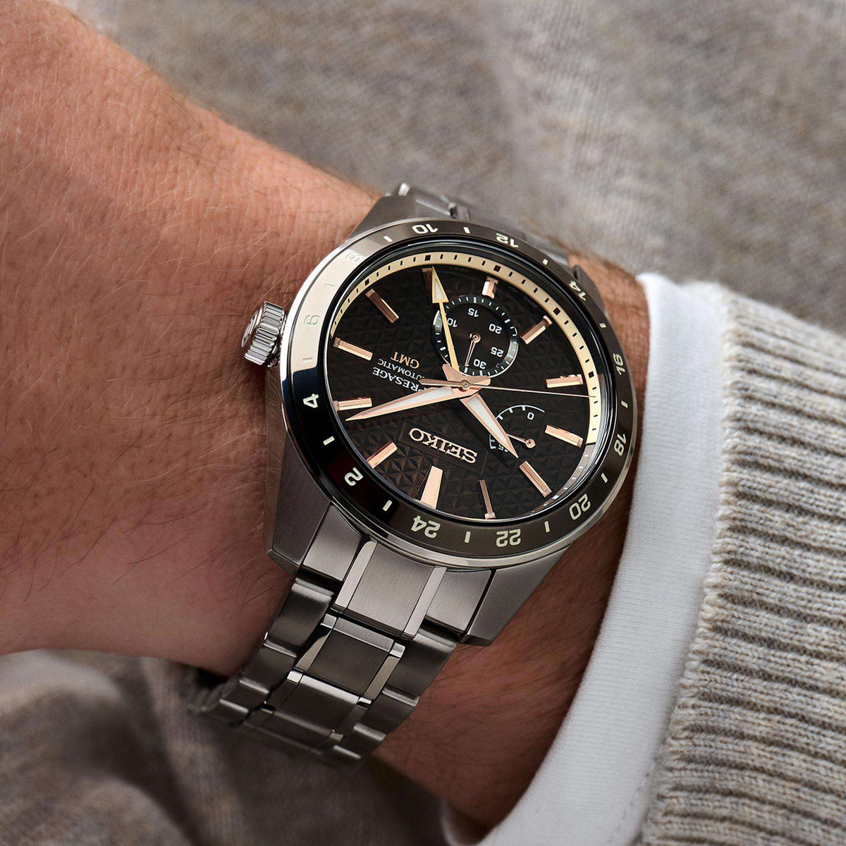 GMT watch on wrist with stainless bracelet, brown dial and black bezel.