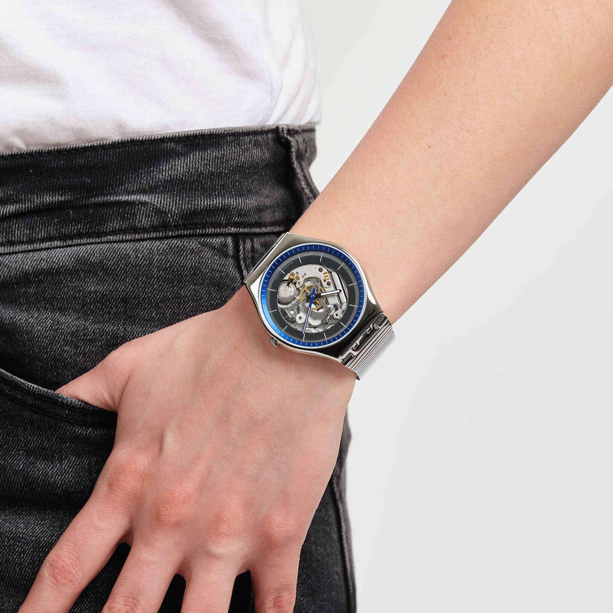 Swatch stainless steel bracelet watch with blue bezel and skeleton dial on wrist