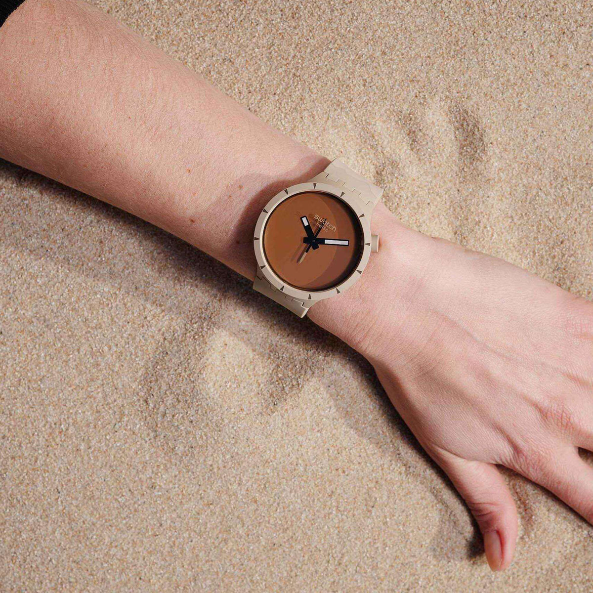 Swatch watch on wrist with beige silicone strap and brown dial, black hands and markers.