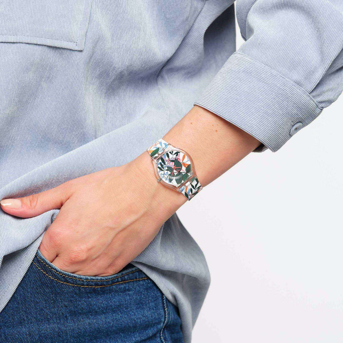 Watch on wrist with multicolor leaf dial and silicone strap; light blue sleeve cuff