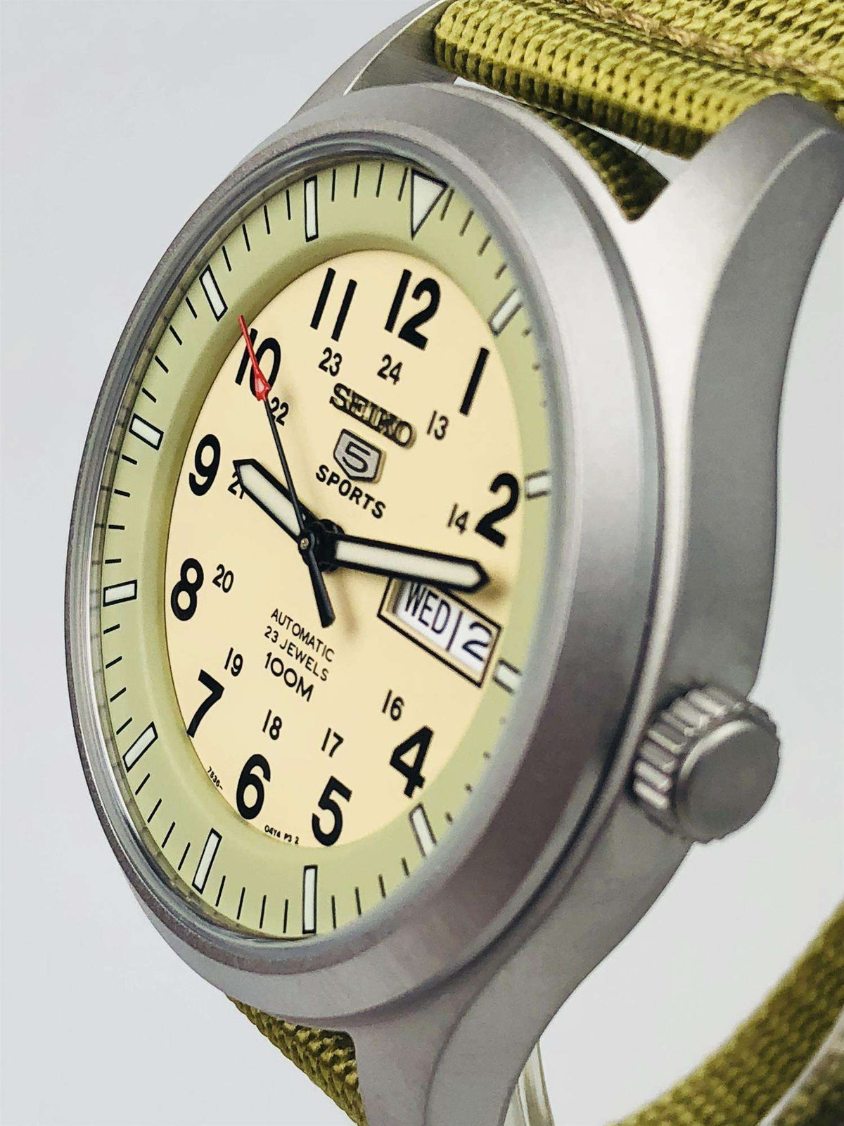 Sports watch side view with cream dial and olive canvas strap; date window at 3 o’clock