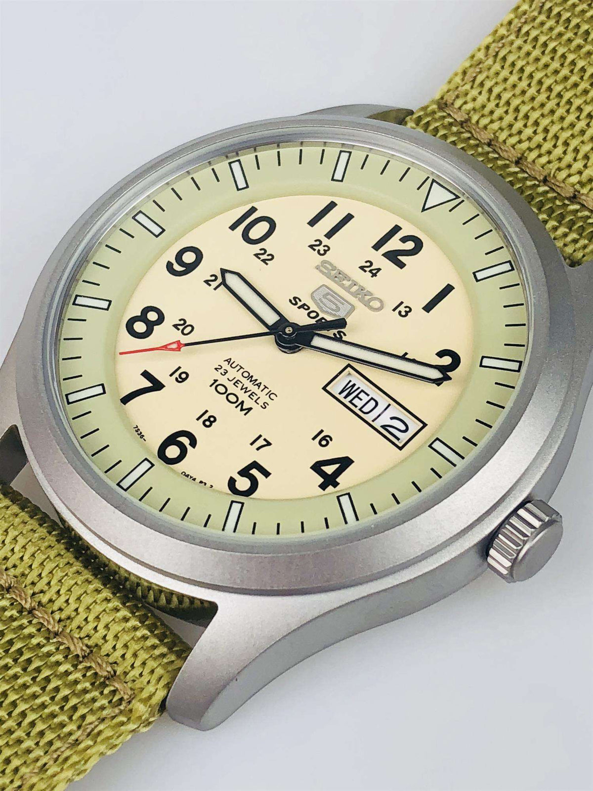 Three-quarter view of sports watch with cream dial, olive strap, and crown on the right