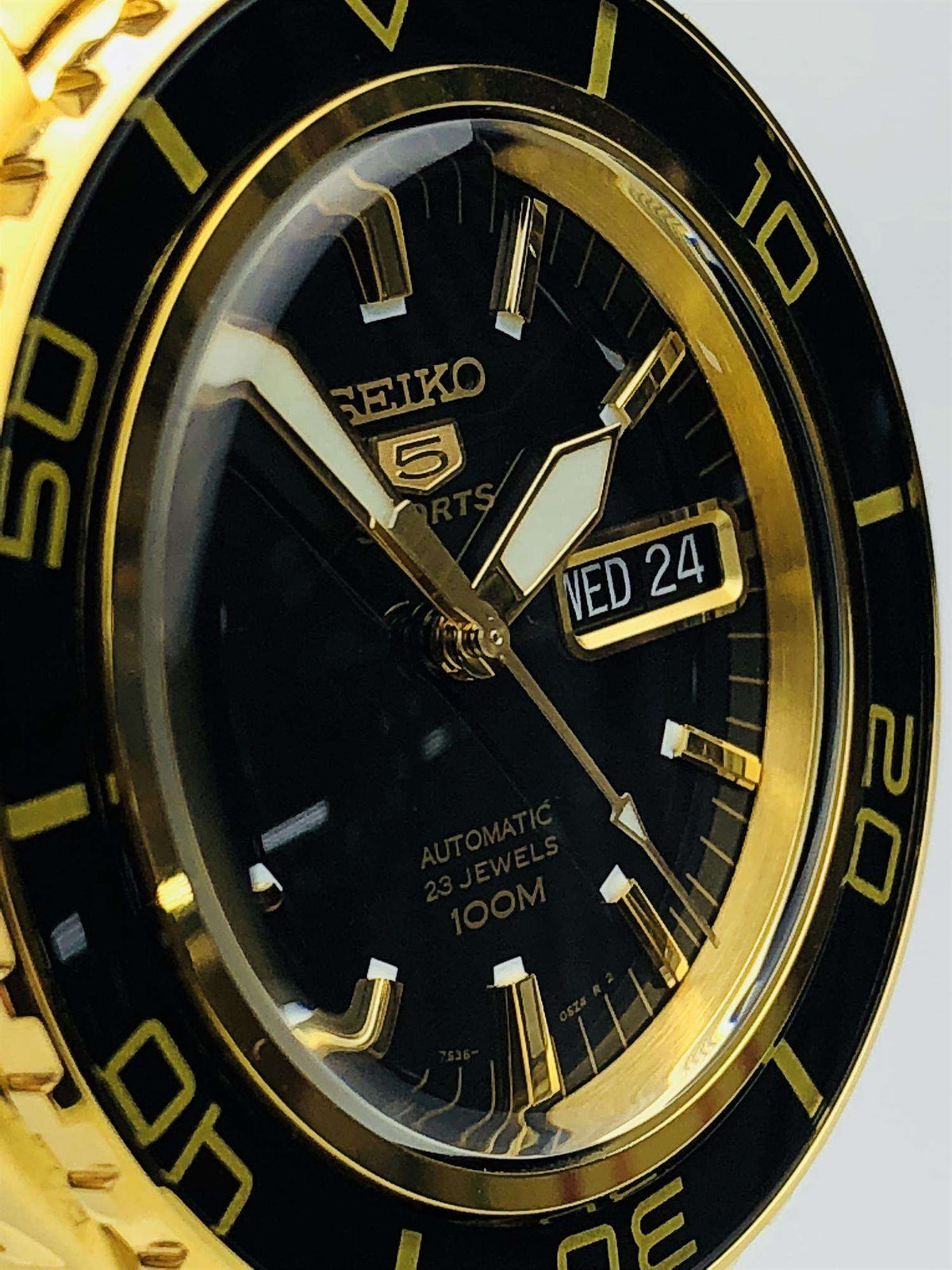 Close-up of gold-tone Seiko 5 Sports black dial with Wed 24 date window and hands