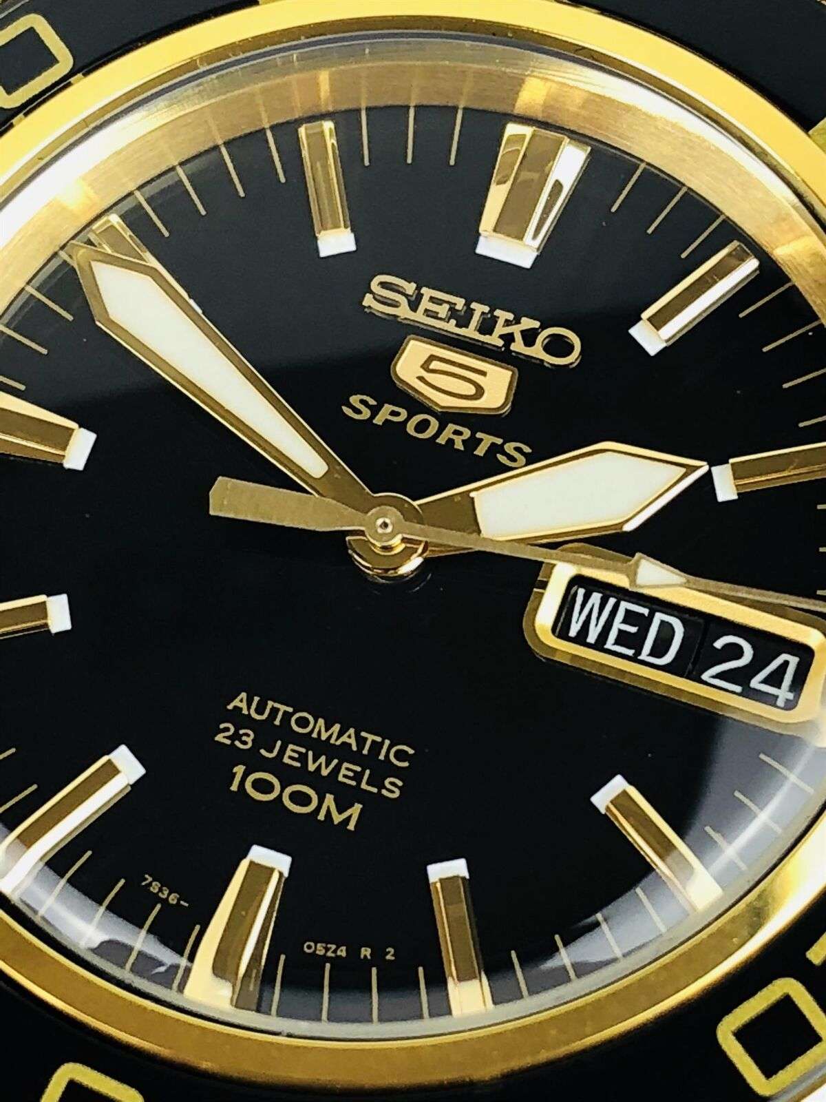 Seiko 5 Sports black dial with gold indices, minute track, and Wed 24 date window
