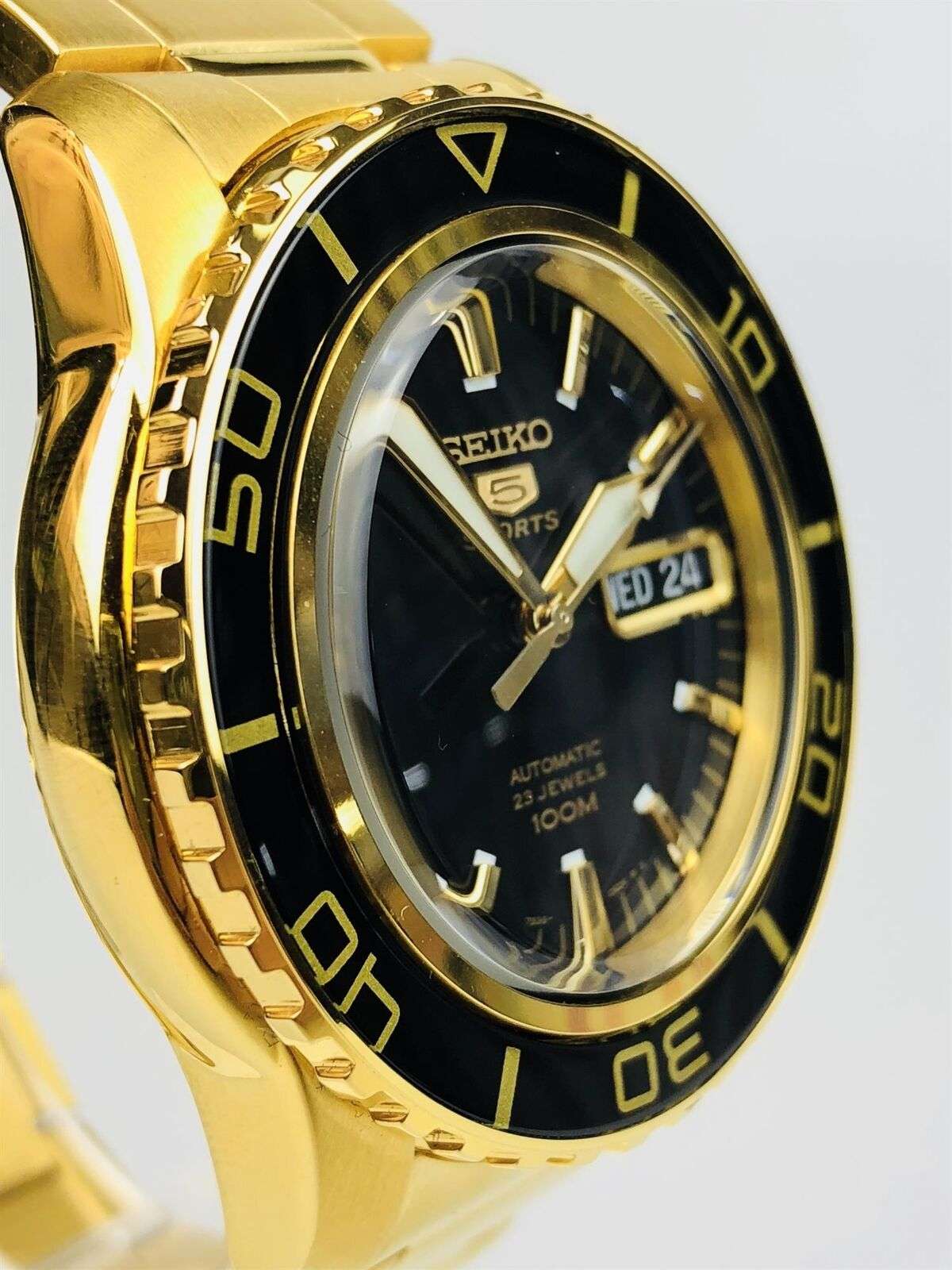 Seiko 5 Sports men's watch side angle close-up, gold bezel and crown, black dial, “WED 24”