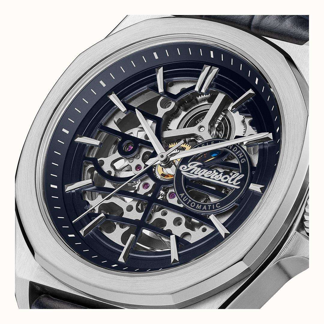 Automatic skeleton dial close-up with silver hands and intricate gears on a navy background.