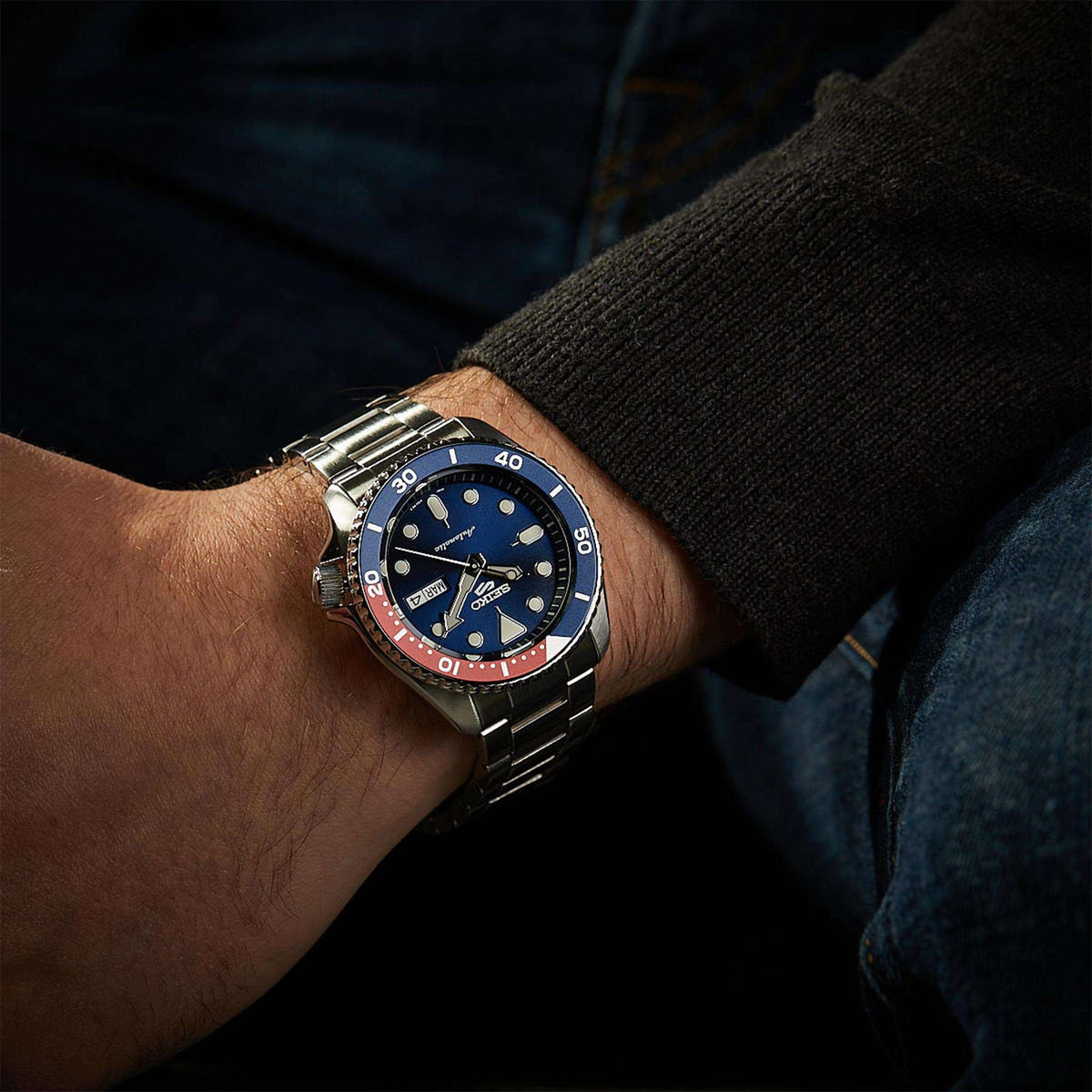 Men's wristwatch with blue dial and red/blue bezel on a stainless steel bracelet