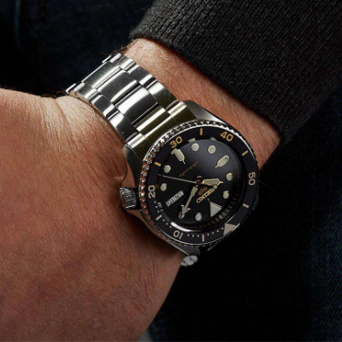 Men's automatic dive watch on wrist, black dial with gold markers, silver metal bracelet