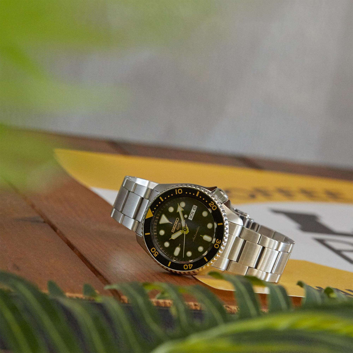 Men's automatic dive watch with black dial, gold hands, silver bracelet, side angle