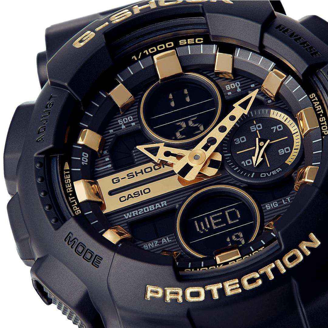 Close-up of black dial with gold bezels, subdials, and date window on watch.