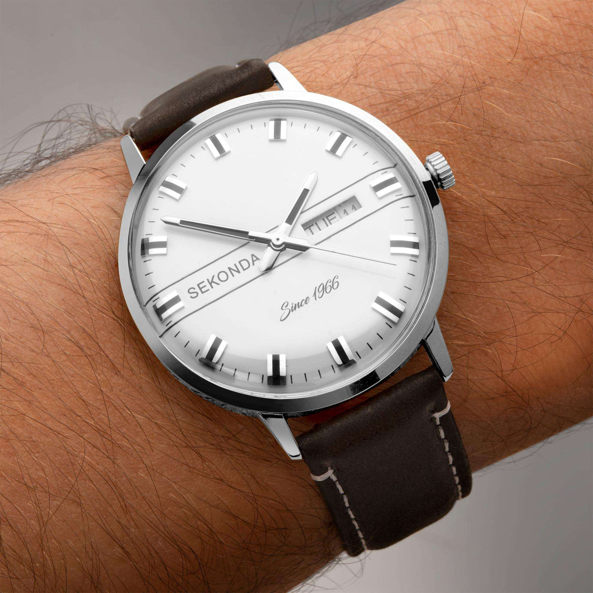Men's wristwatch with white dial and black leather strap worn on bare arm