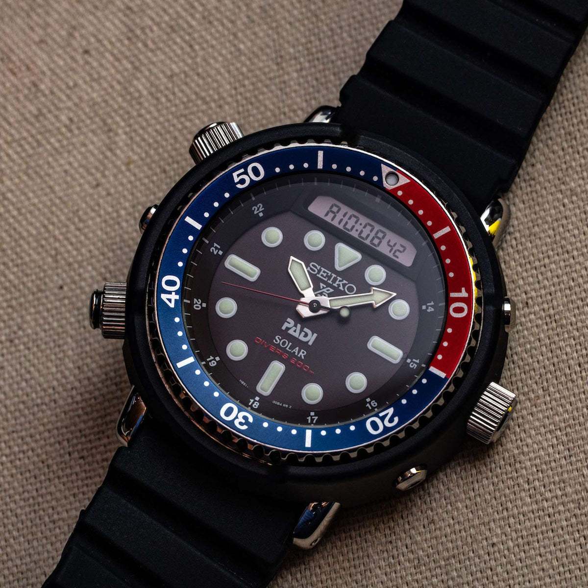 Men's Seiko solar dive watch, close-up of black dial, blue-red bezel, black strap.
