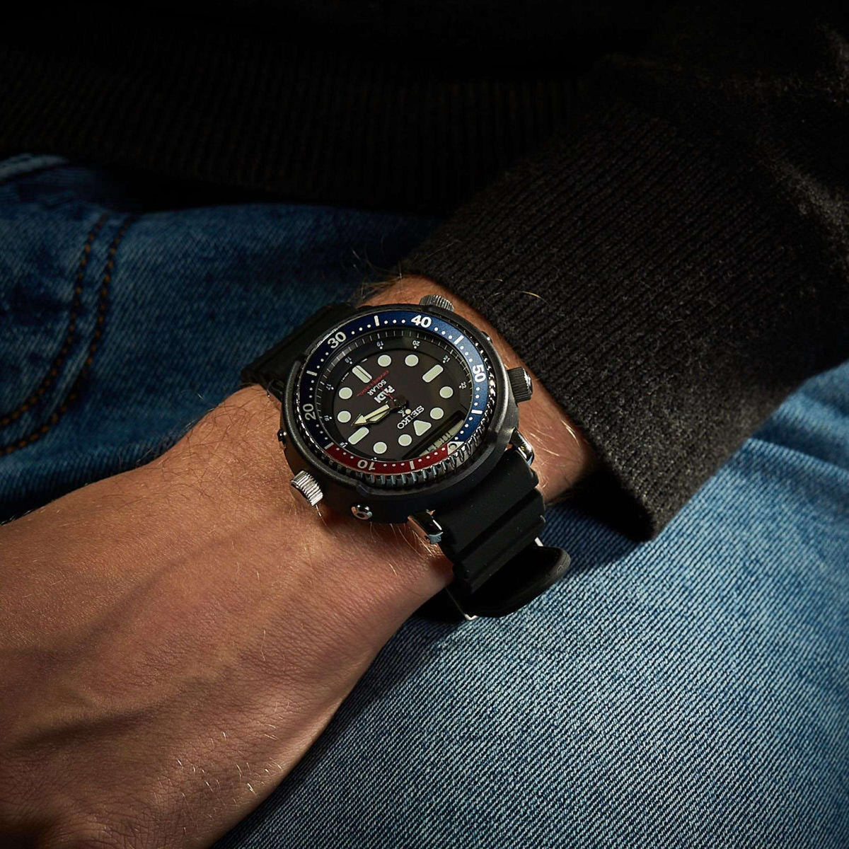 Men's Seiko dive watch worn on wrist, black dial with blue-red bezel and black strap.