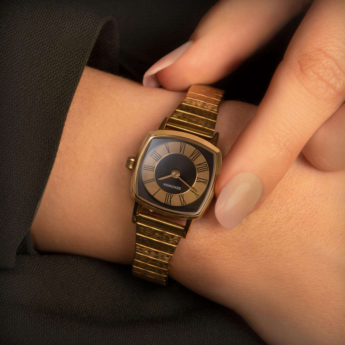 Gold-tone ladies wrist watch with black dial and metal bracelet on wrist