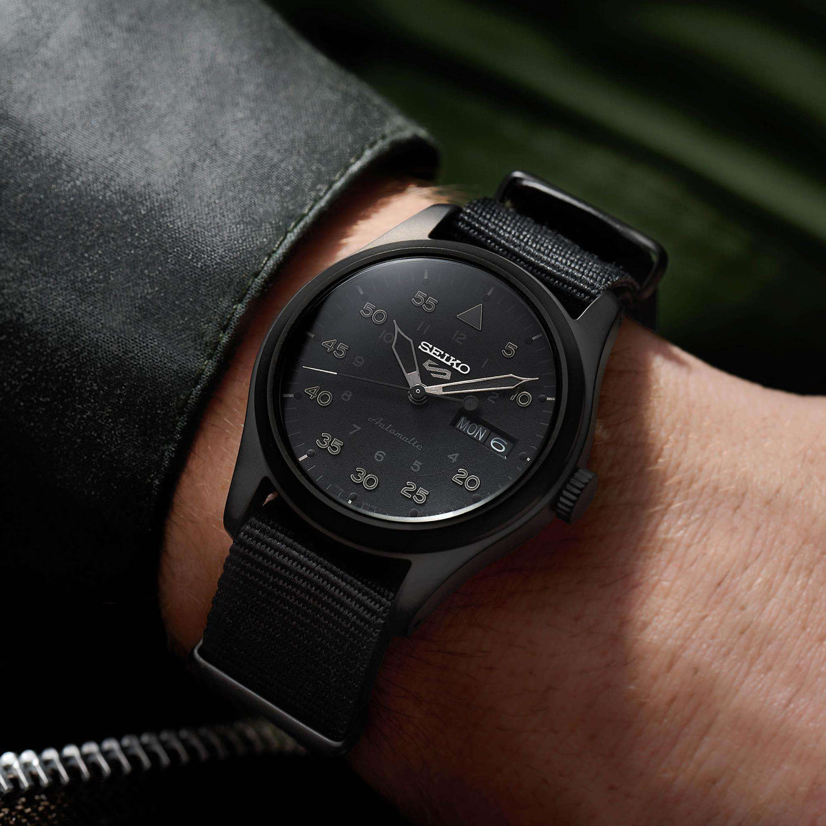 Men's black automatic field watch on wrist, black dial with day-date window
