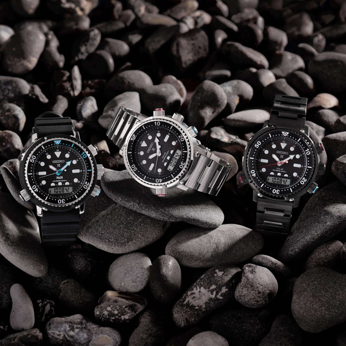 Three stainless steel diver watches with black dials, rotating bezels, and colored accents