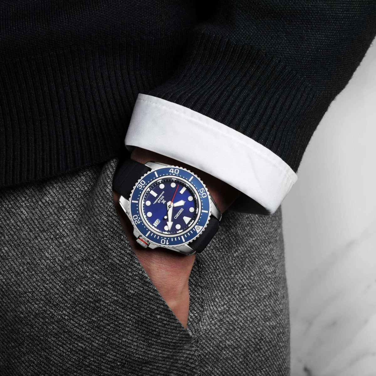Men's solar diver watch on wrist with blue dial, black rubber strap, black knit cuff