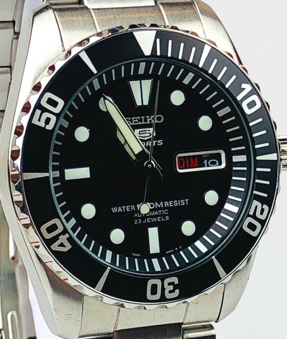 Close-up of black dial men’s dive watch with light markers, hands, and date window