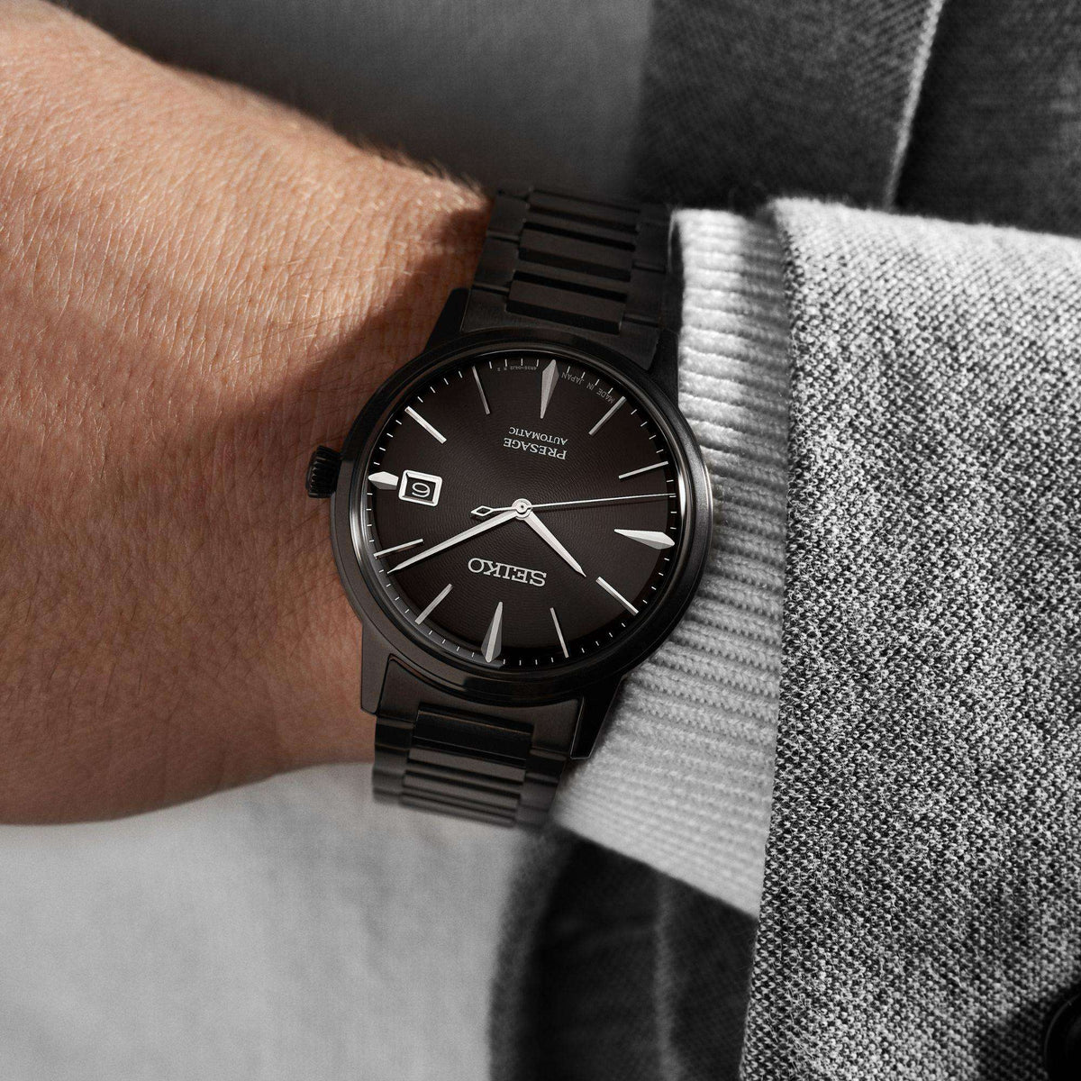 Black dial automatic wristwatch with black metal bracelet worn on wrist