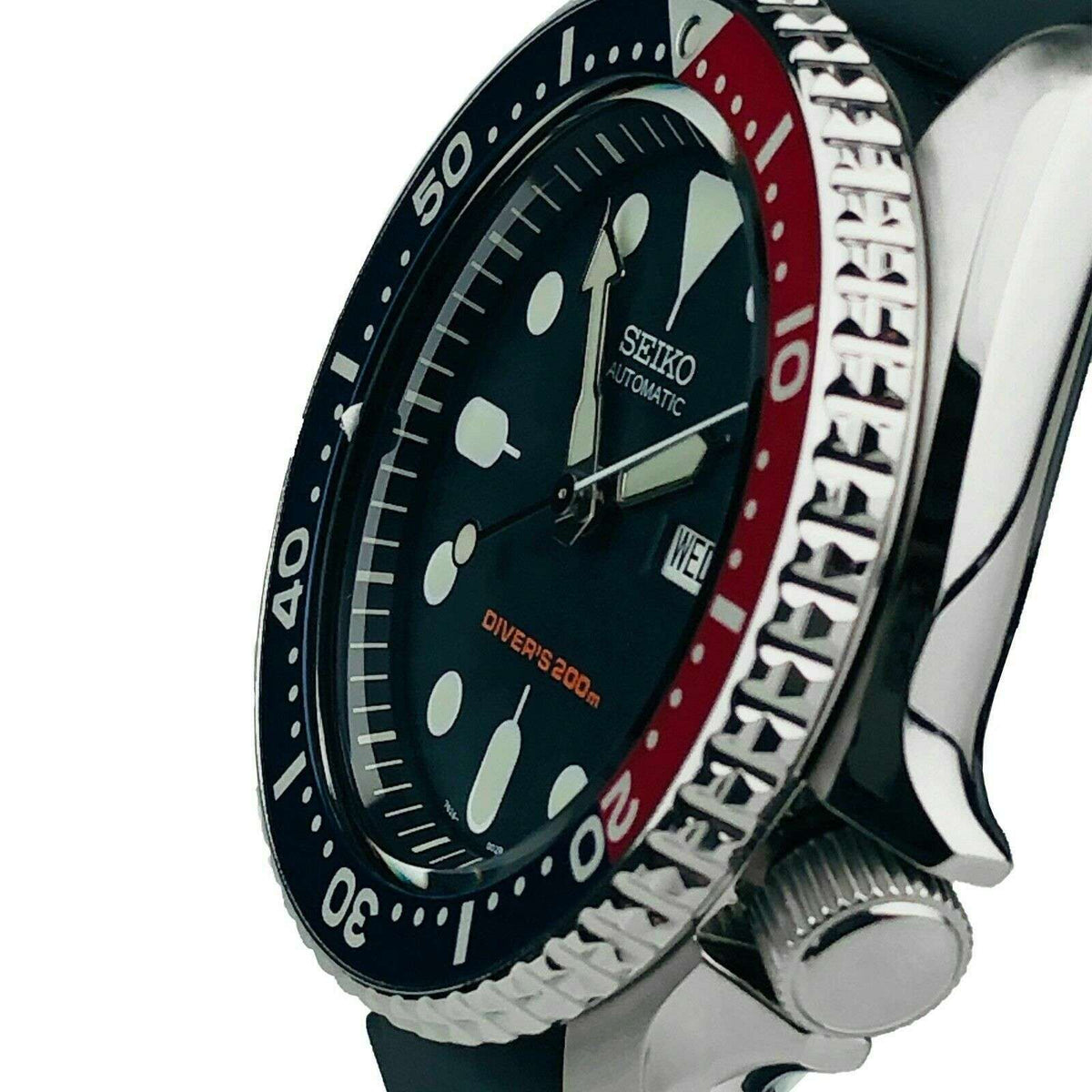 Automatic dive watch close-up with black dial, red/blue bezel ring, and day/date window