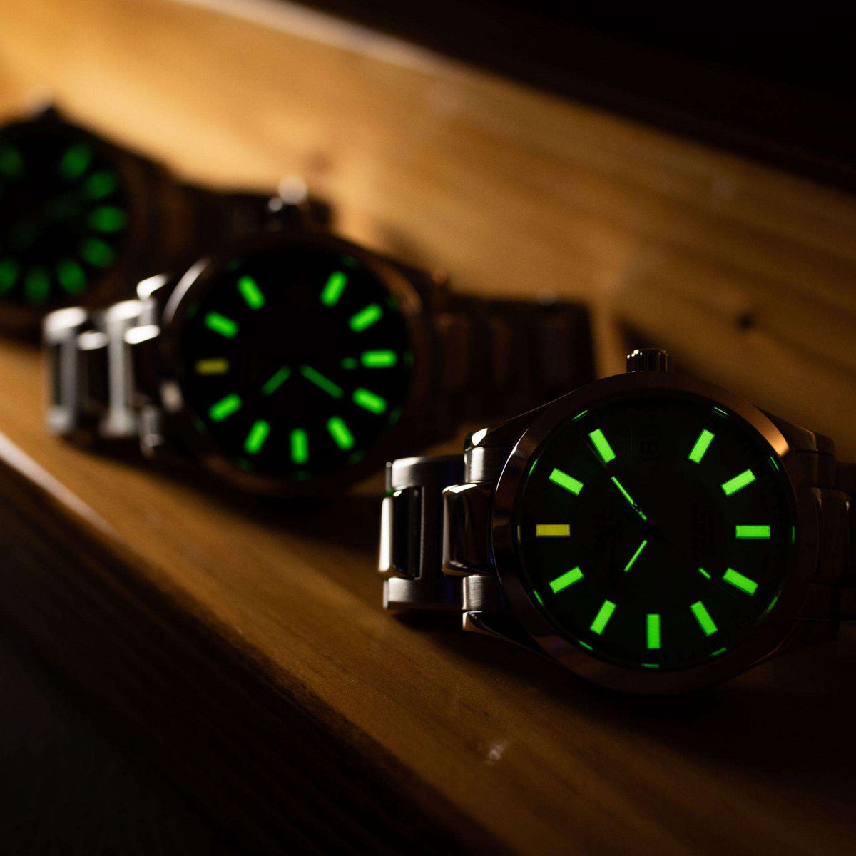 Dark wristwatch with green glowing markers and subdial details, stainless bracelet
