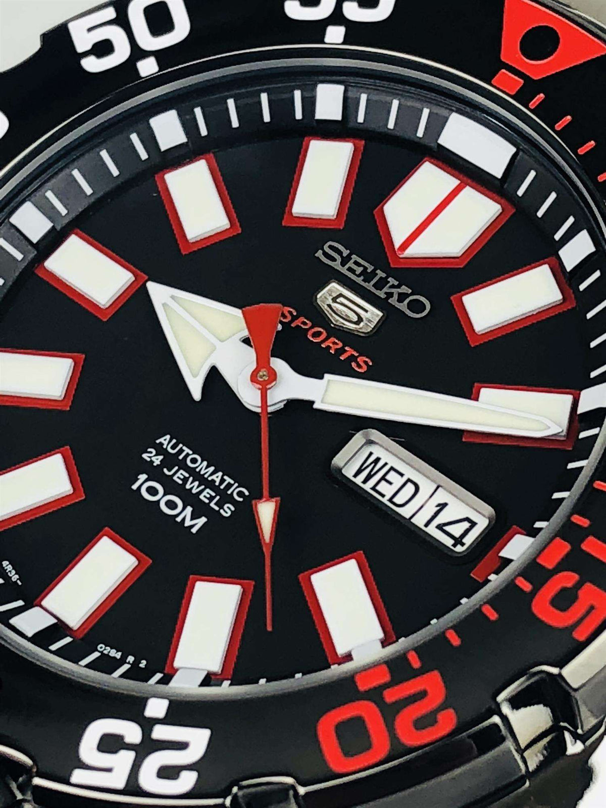 Seiko Sports watch dial close-up with white hour markers, red hands, and WED14