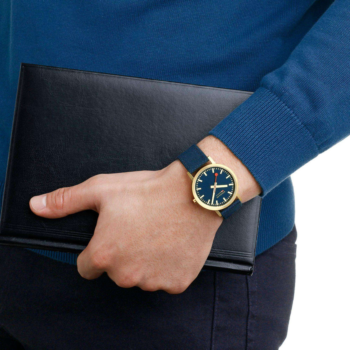 Gold-tone Mondaine watch with deep blue dial and blue fabric strap on wrist