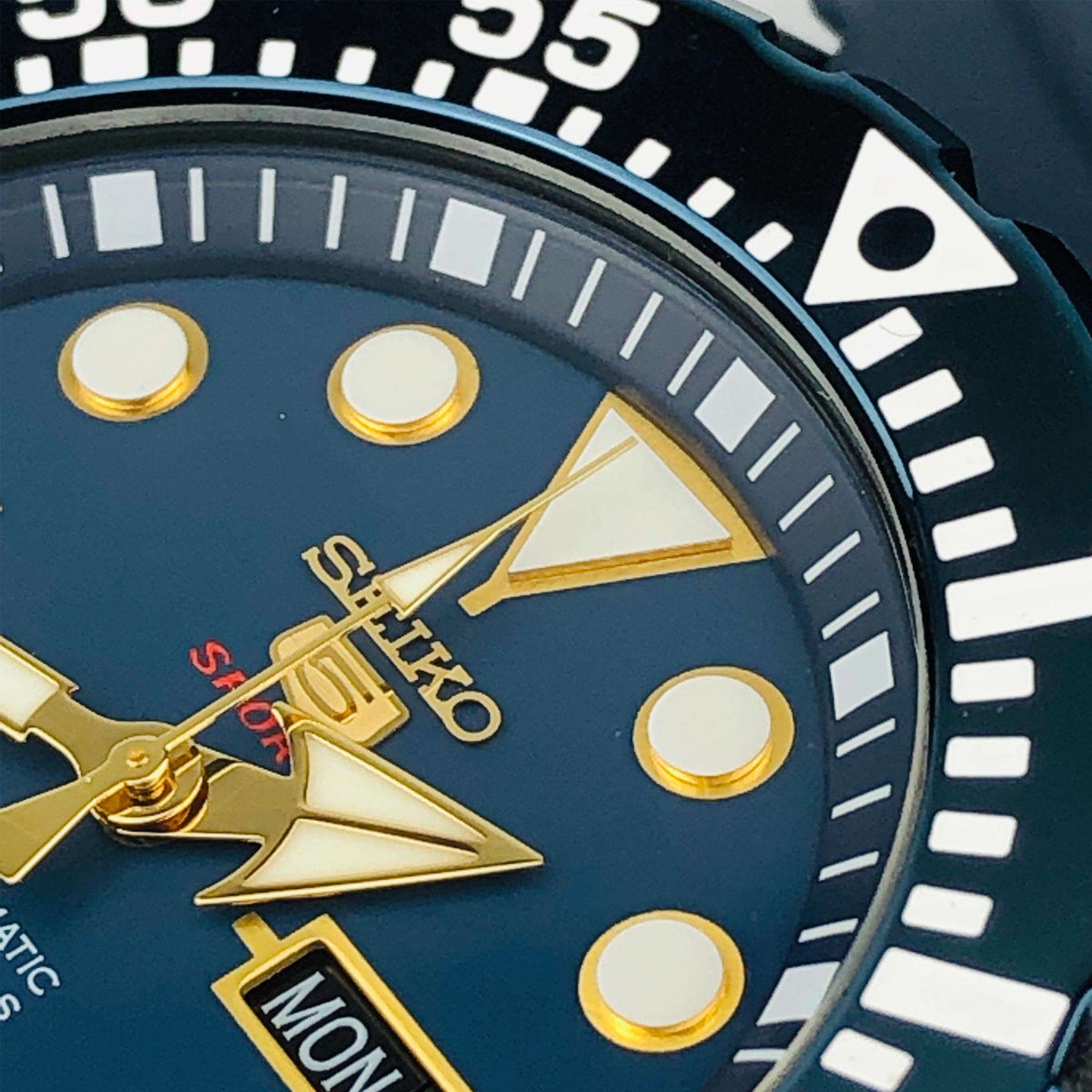 Seiko 5 Sports watch dial close-up with blue face, gold markers, and date window