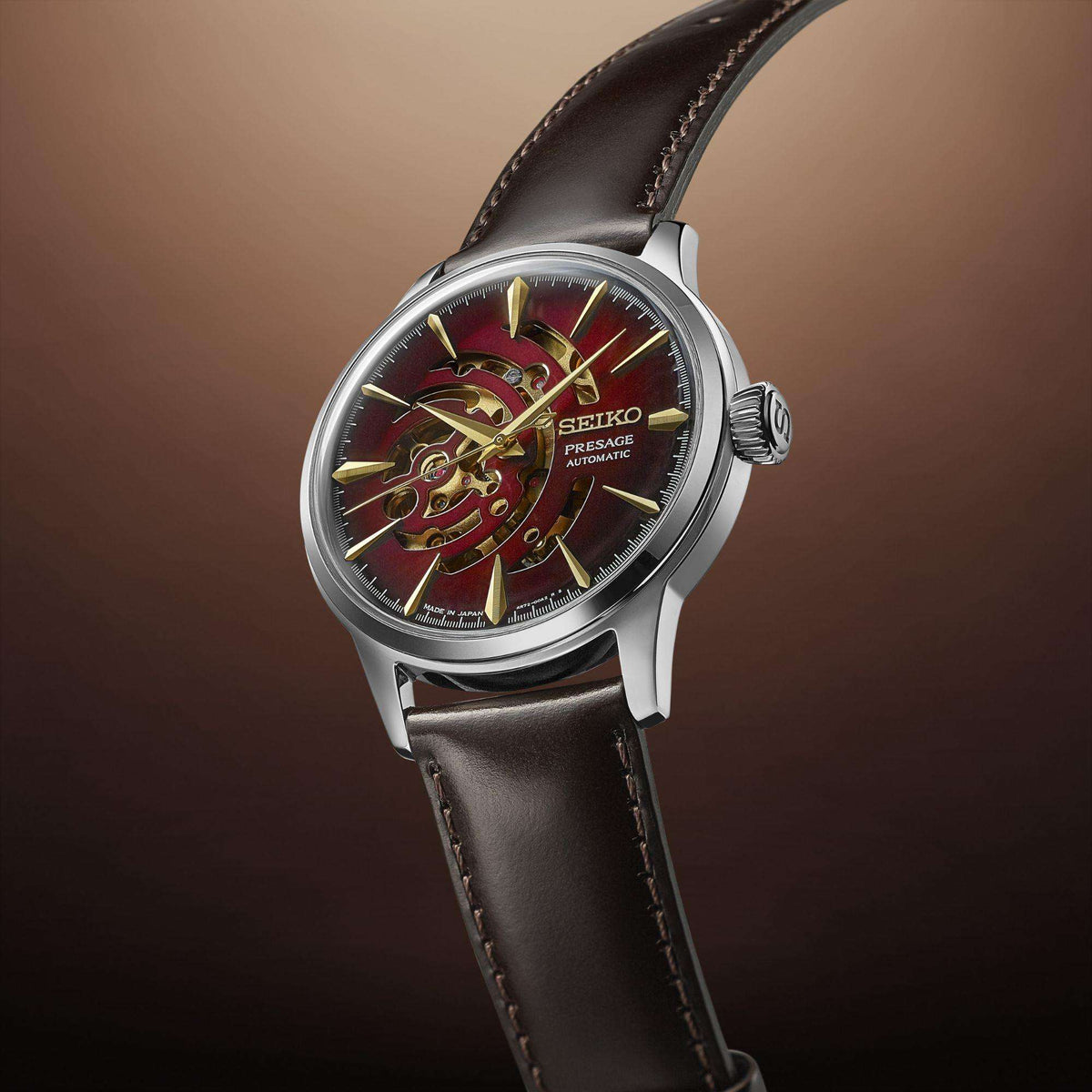 Men's automatic watch with red dial, gold-tone skeleton hands, black leather strap.