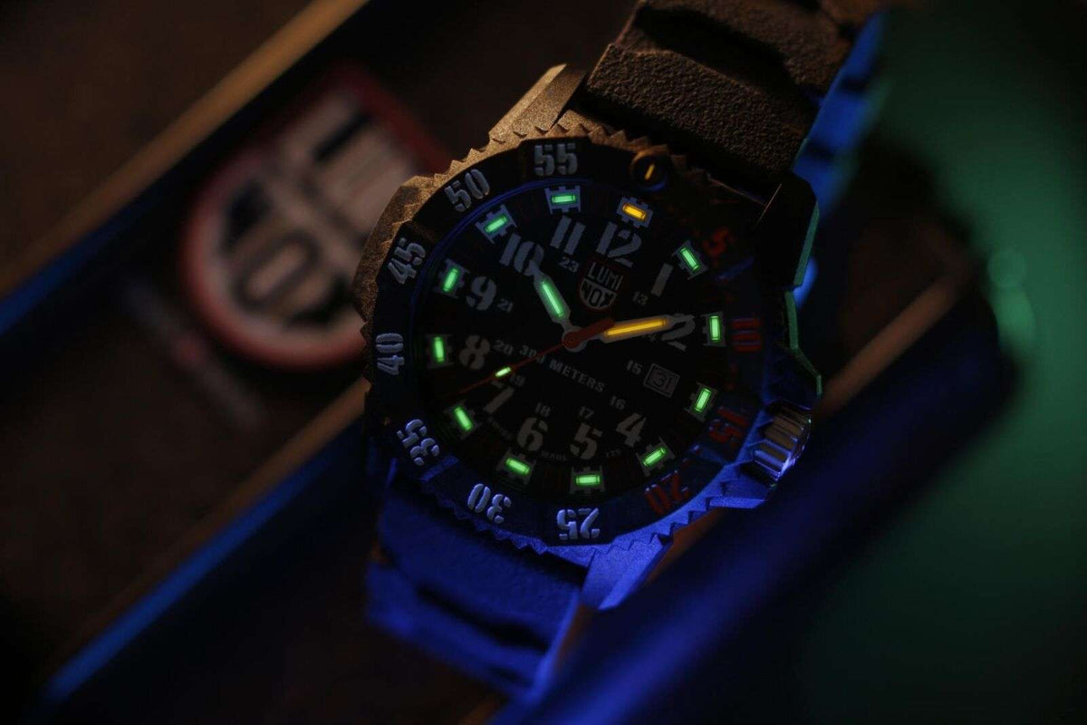 Dark-lit carbon watch showing green and orange luminous dial markings on black strap.