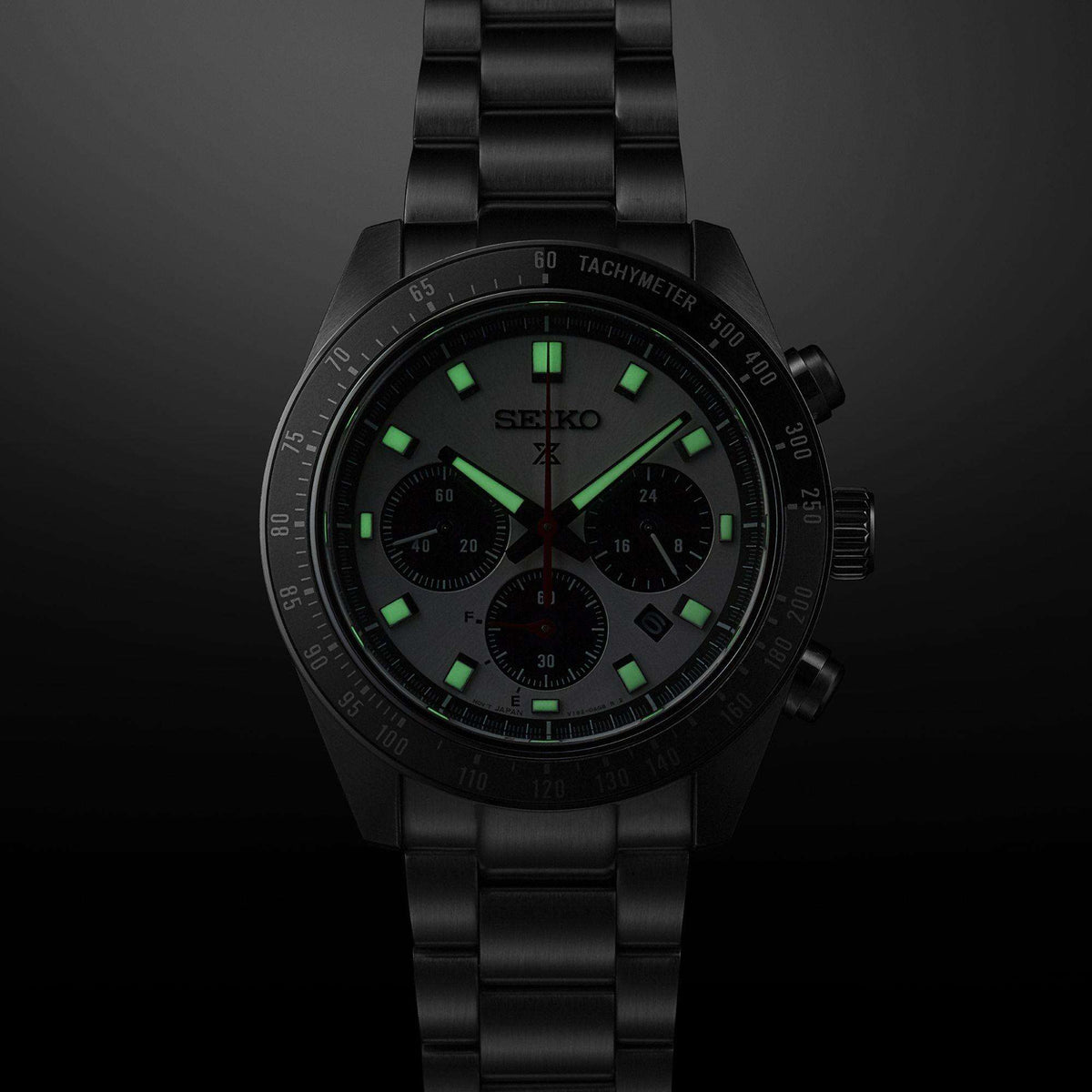 Black chronograph watch with green markers, silver-toned hands, tachymeter bezel, and three subdials