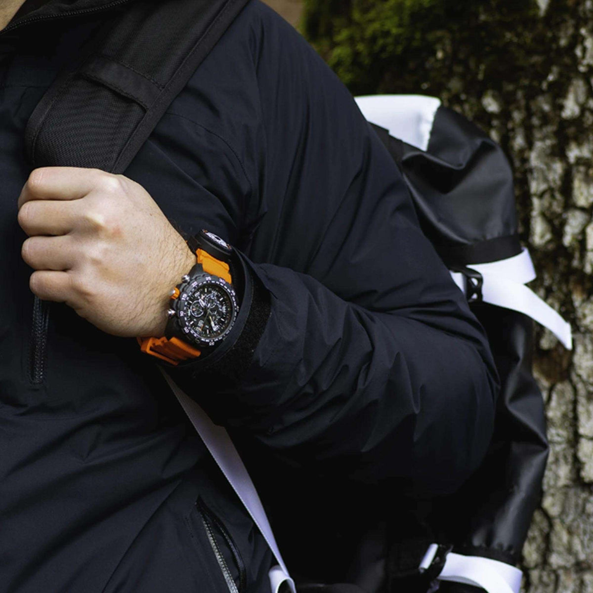 On-wrist outdoor view of the Luminox Bear Grylls XB.3749 survival watch with orange strap worn by a hiker with a backpack